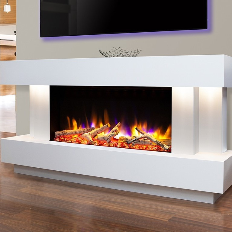 A modern white fireplace with an electric flame effect over realistic looking logs. The fireplace is installed on a light grey wall. The floors are wooden. Above the fireplace there is a large screen TV with a purple backlight. 